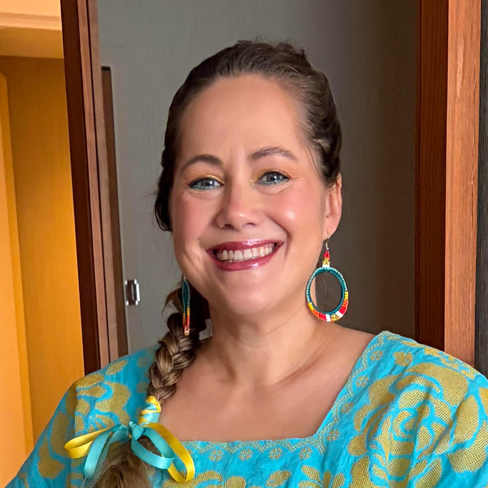 author with single braid with yellow and blue ribbons and beaded hoop earrings